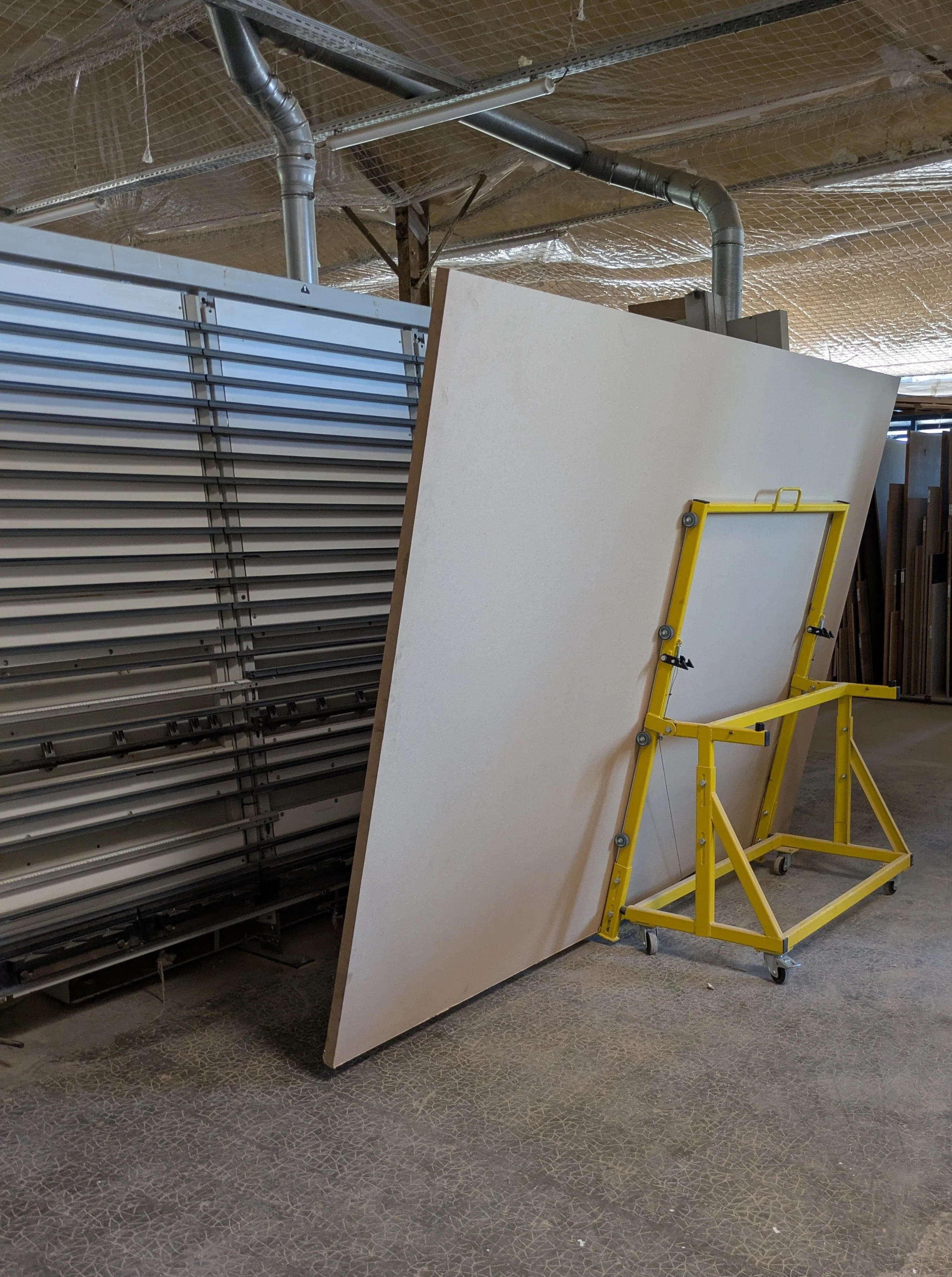 Le chariot Flipanel chargé d'un panneau debout, à côté du stock de panneaux de l'atelier